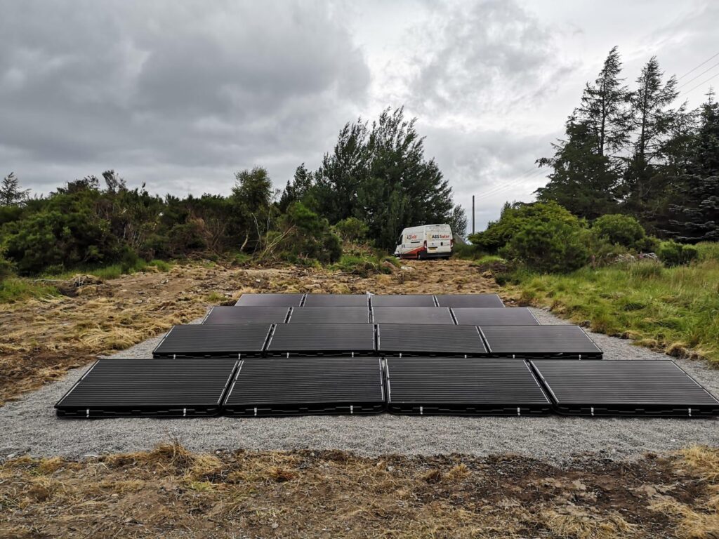 16 solar panels in a cleared wooded area with a white van in the background