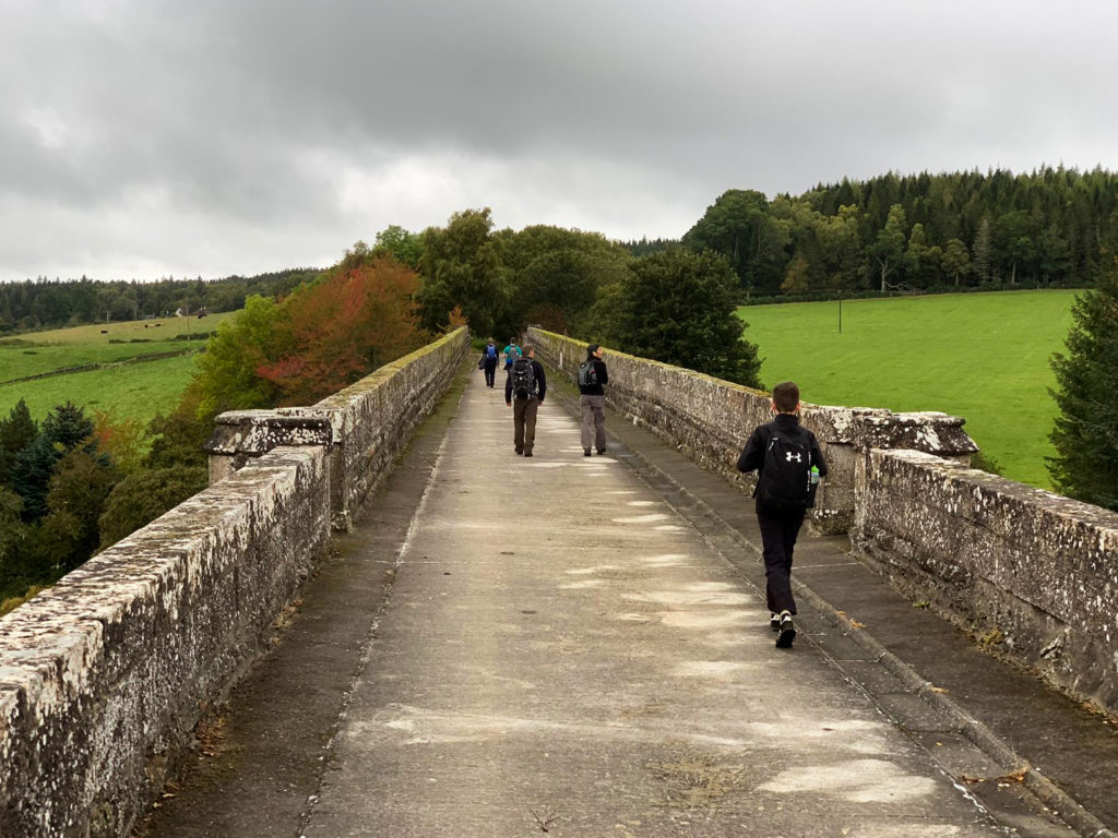 Figures in the distance walk over a large stone bridge 