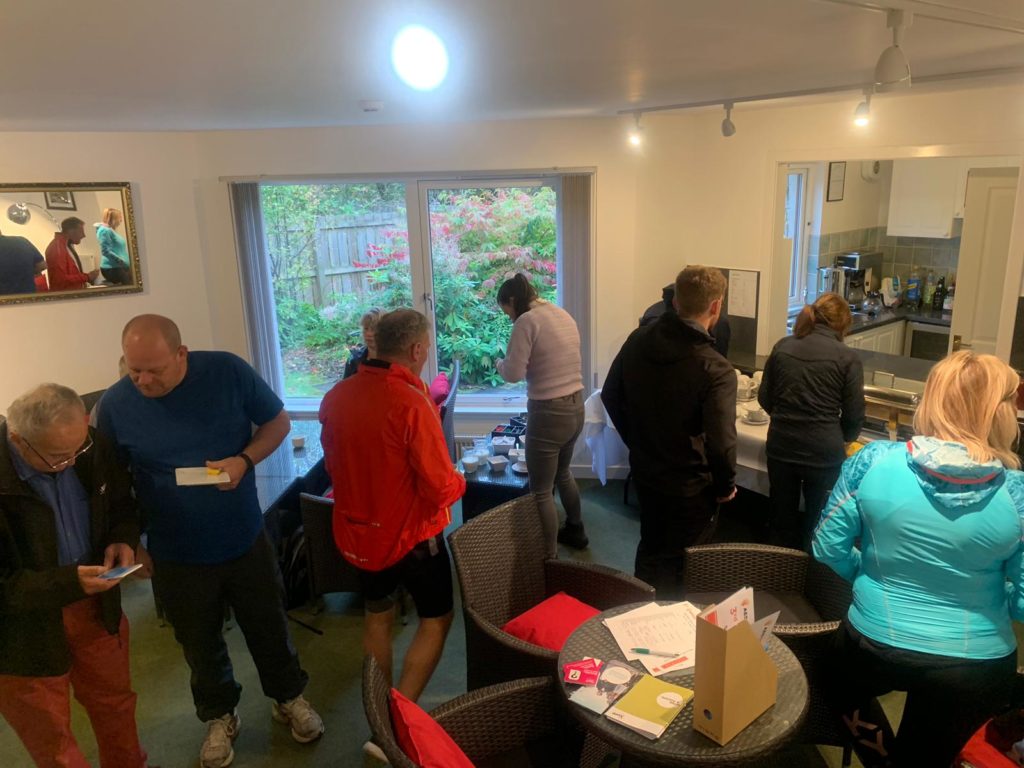 A group of people stand in a room discussing plans and making coffee