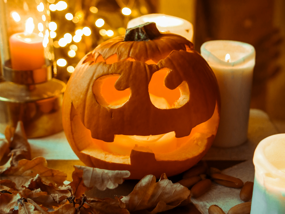 Green Halloween in 2023 Jack O' Lantern surrounded by dried autumn leaves, acorns and, candles and fairy lights.