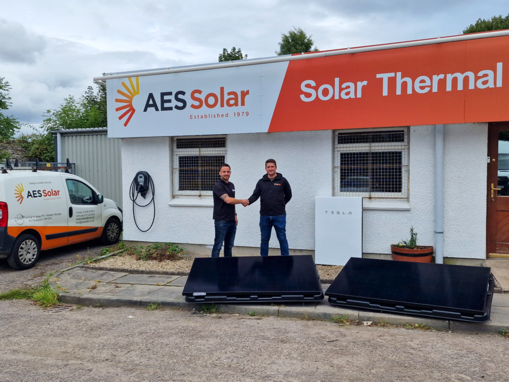 Two men shake hands outside a building with two solar panels in front of them as we're shining a light on 2023